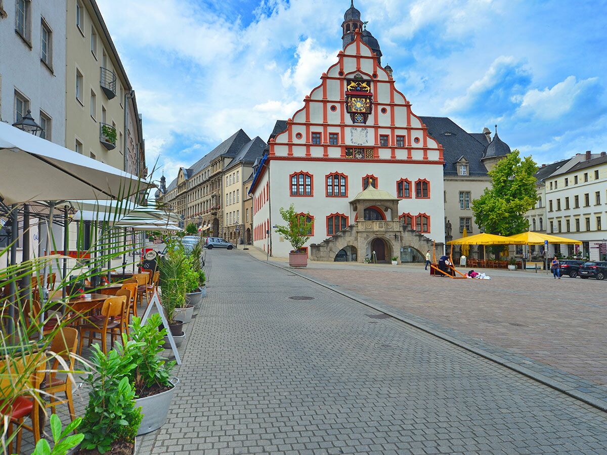 Blick auf das historische Rathaus in einem deutschen Stadtzentrum mit Marktplatz, Außencafés und Gebäuden unter blauem Himmel.