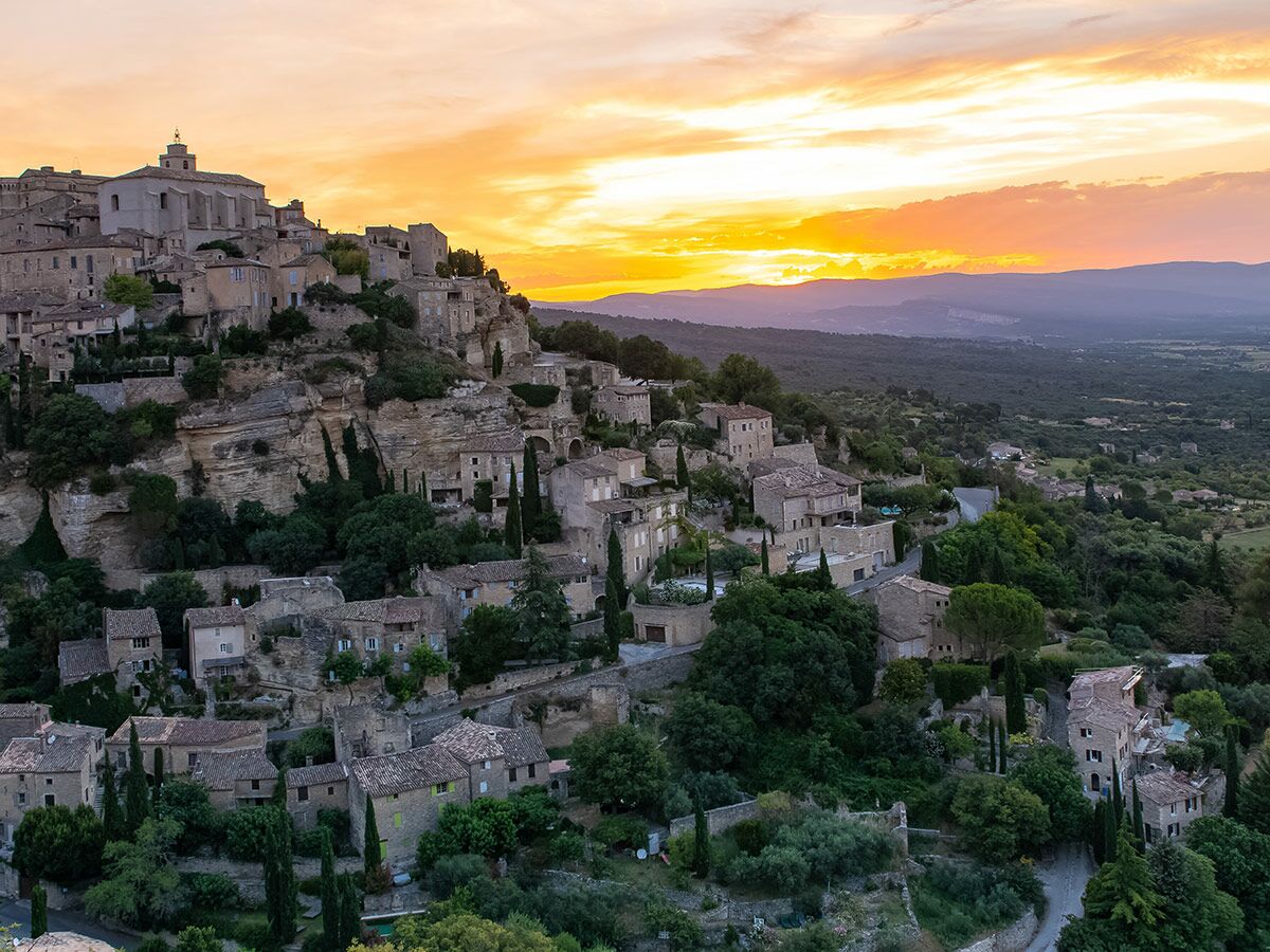 Panoramablick auf ein historisches Bergdorf in der Provence, Frankreich, bei Sonnenuntergang mit warmen Himmelsfarben.