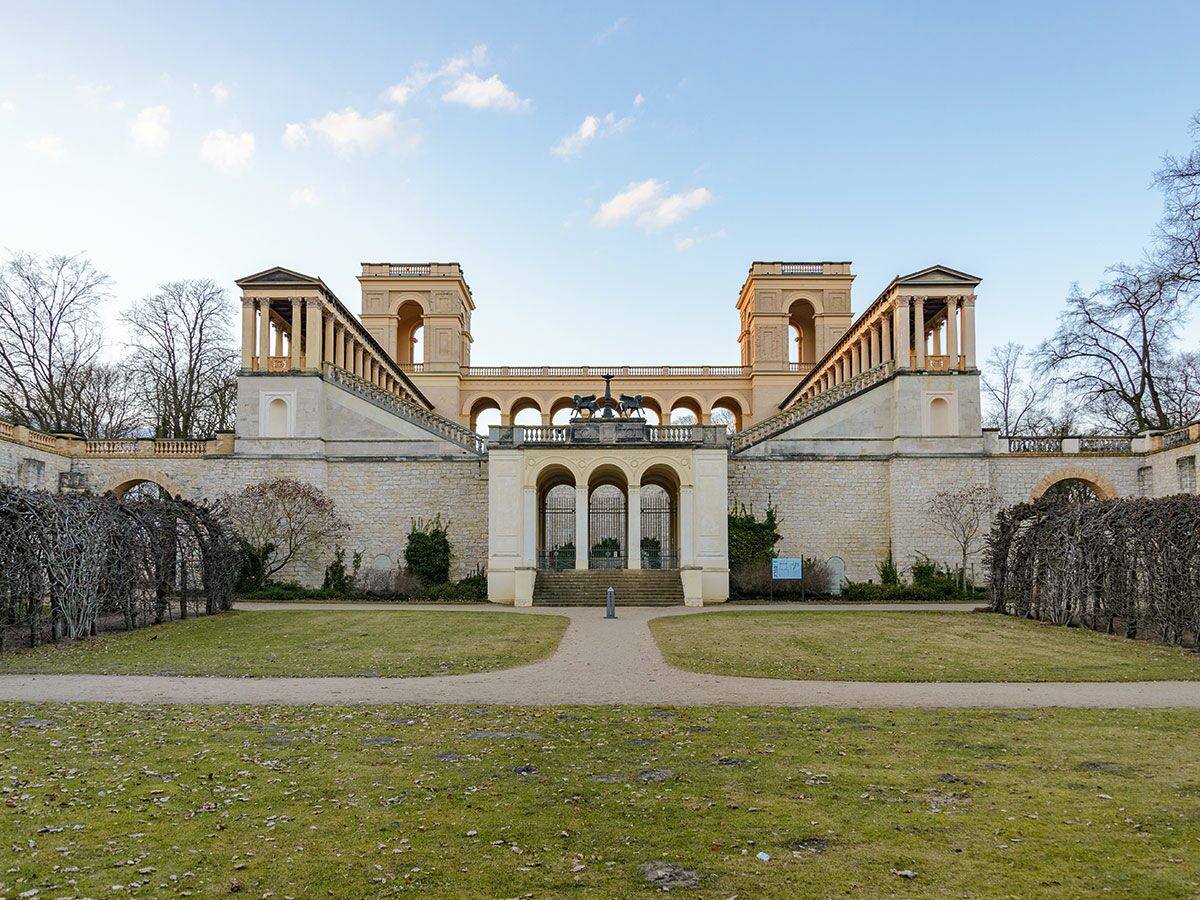 Historisches Orangerieschloss im Sanssouci Park Potsdam mit symmetrischer Architektur, Säulen, Treppen, Bögen und einer Quadriga-Statue.