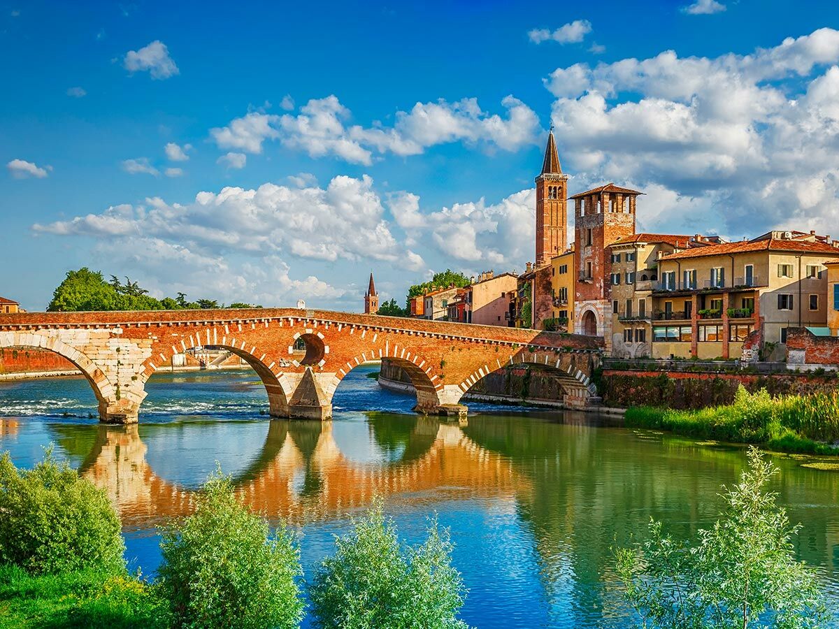 Historische Ponte Pietra Brücke über den Fluss Etsch in Verona, Italien, mit Altstadt und blauem Himmel.
