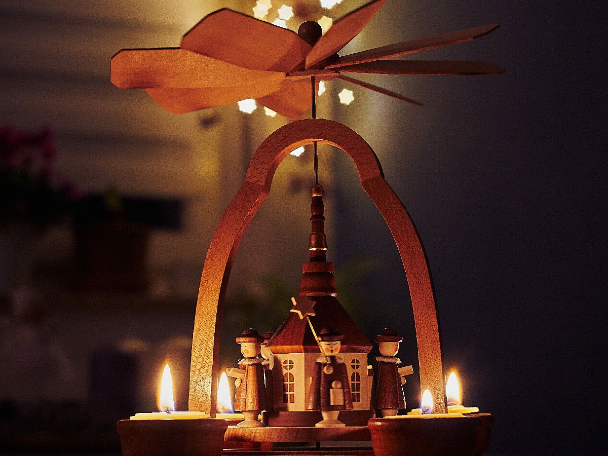 Detailaufnahme einer traditionellen hölzernen Weihnachtspyramide mit drei brennenden Kerzen und geschnitzten Figuren im warmen Licht.