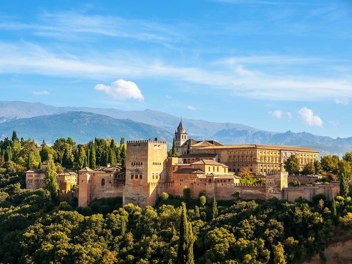 Panoramablick auf die prächtige Alhambra in Granada, eine historische Palastfestung umgeben von grünen Bäumen unter blauem Himmel.