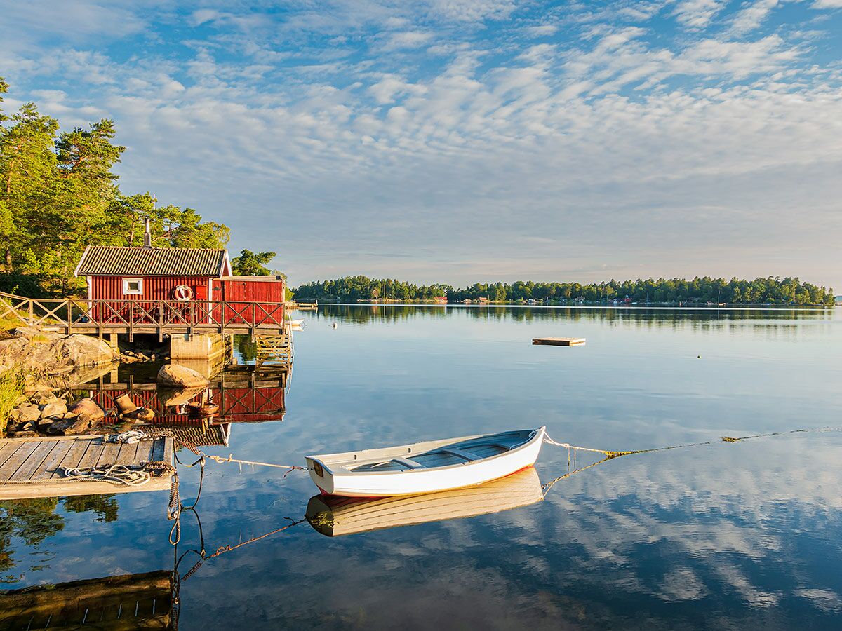 Rote Fischerhütte am See mit Steg und Ruderboot; ruhige Naturlandschaft im Sommer.