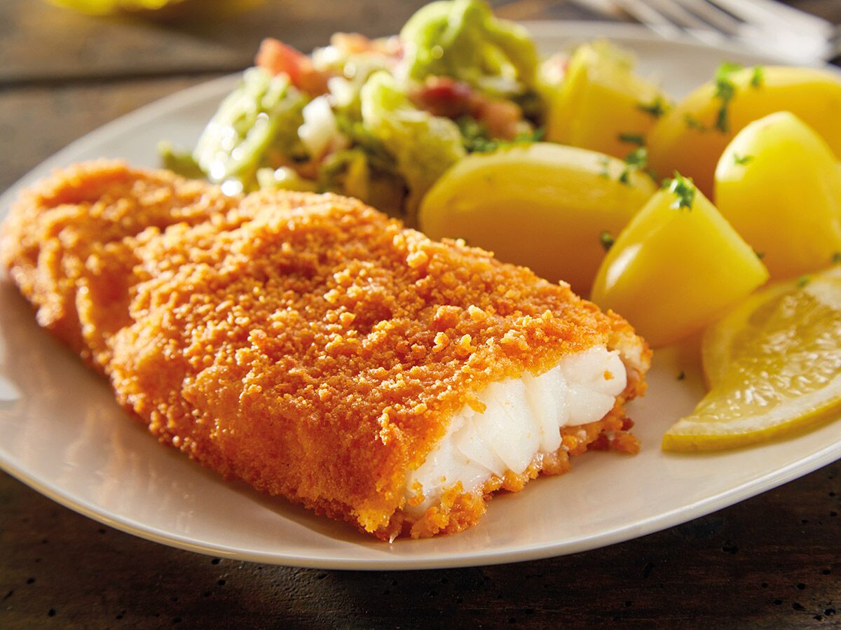 Knuspriges, paniertes Fischfilet mit Salzkartoffeln, frischem grünen Salat und Zitronenspalten auf einem weißen Teller angerichtet.