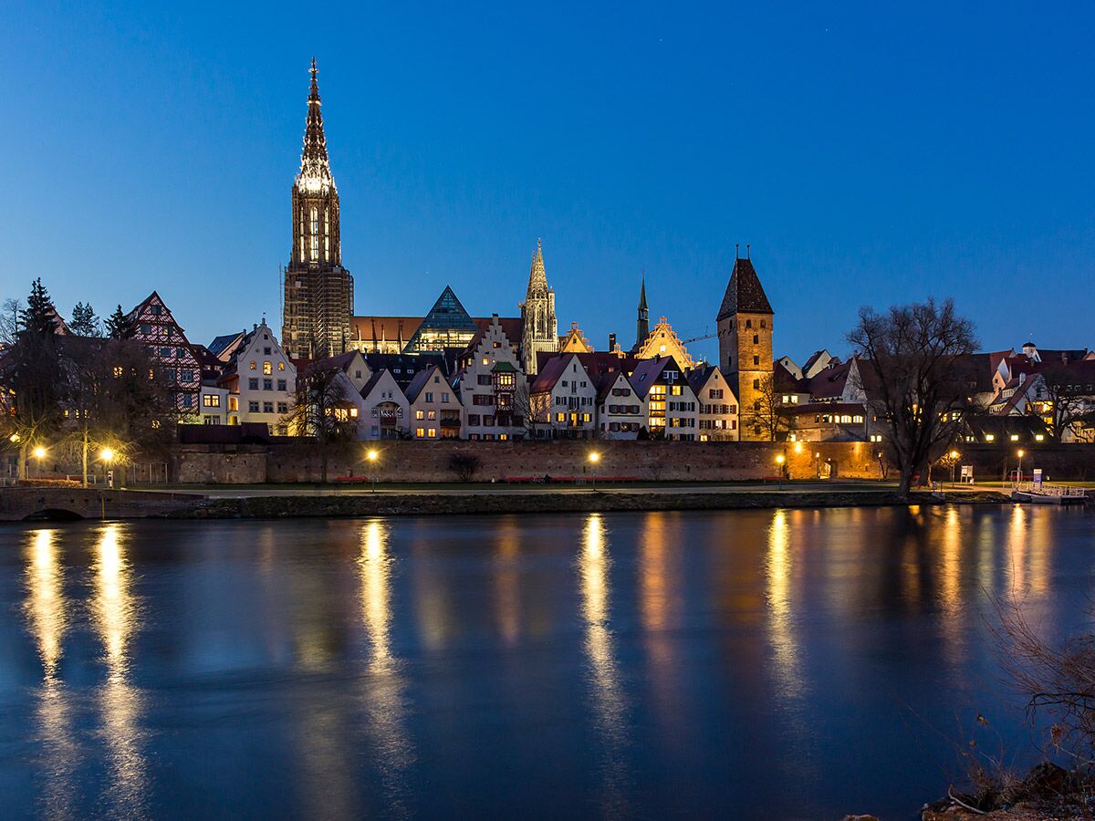 Ulm bei Nacht: Beleuchtetes Ulmer Münster, Altstadthäuser und Metzgerturm spiegeln sich malerisch in der Donau.