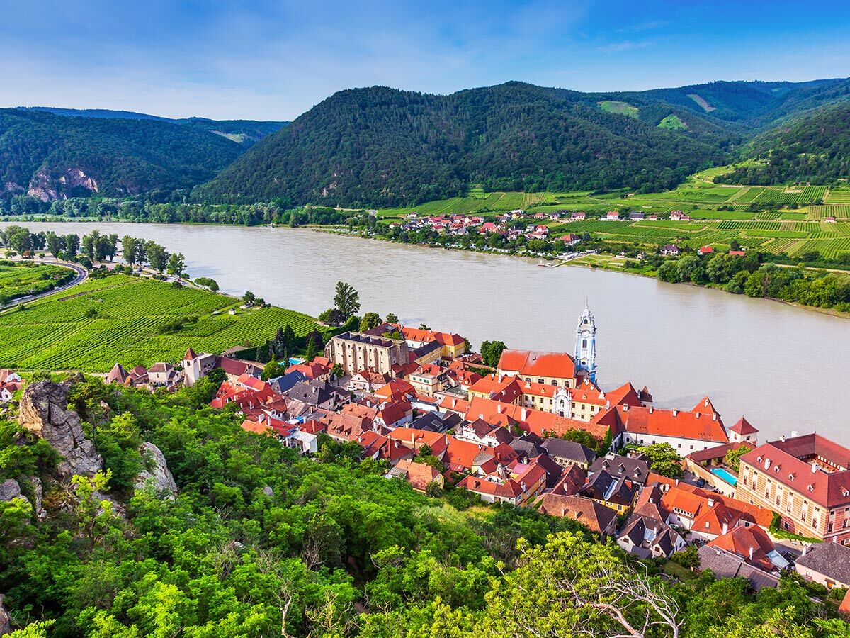 Malerisches Dürnstein in der Wachau, Österreich, mit Dorf, Donau, Weinbergen und Hügeln unter blauem Himmel.