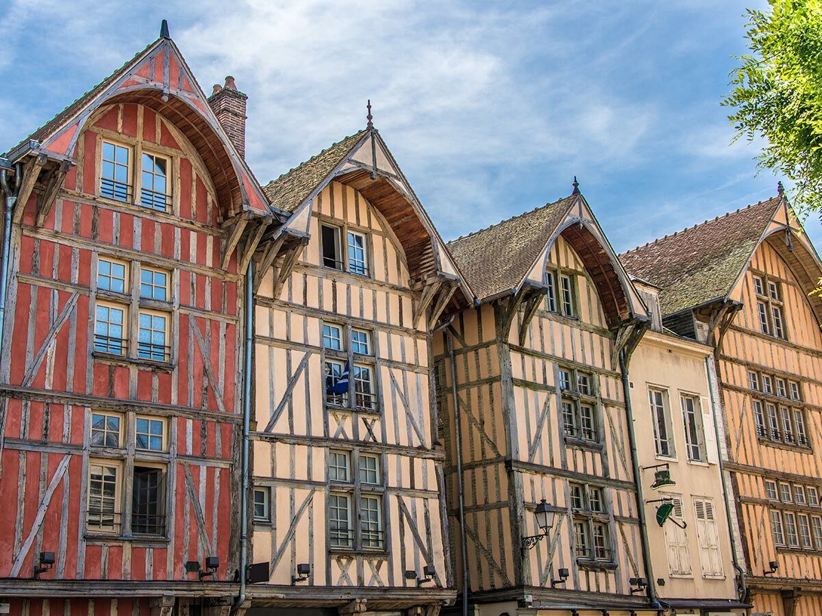 Reihe farbiger historischer Fachwerkhäuser unter blauem Himmel, mit steilen Dächern und vielen Fenstern. Charakteristische Architektur.