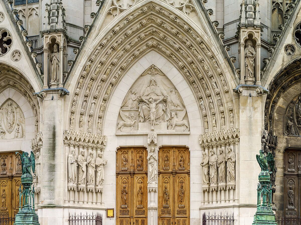 Prächtige gotische Kirchenfassade mit zentralem Bogenportal, Skulpturen der Kreuzigung, Heiligenstatuen und geschnitzten Holztüren.
