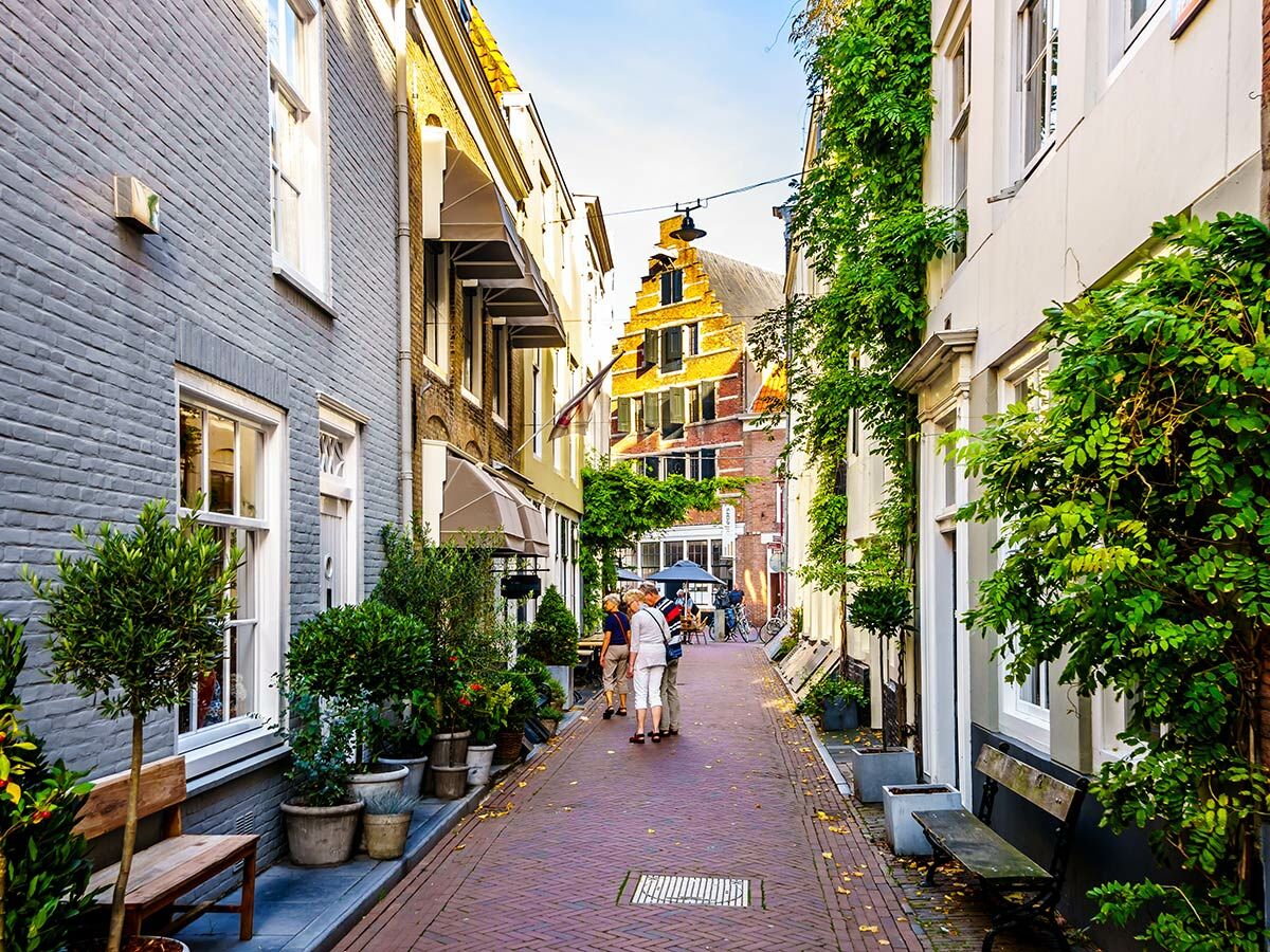 Malerische, enge Gasse mit alten Backsteinhäusern, grünen Pflanzen und Spaziergängern an einem sonnigen Tag.