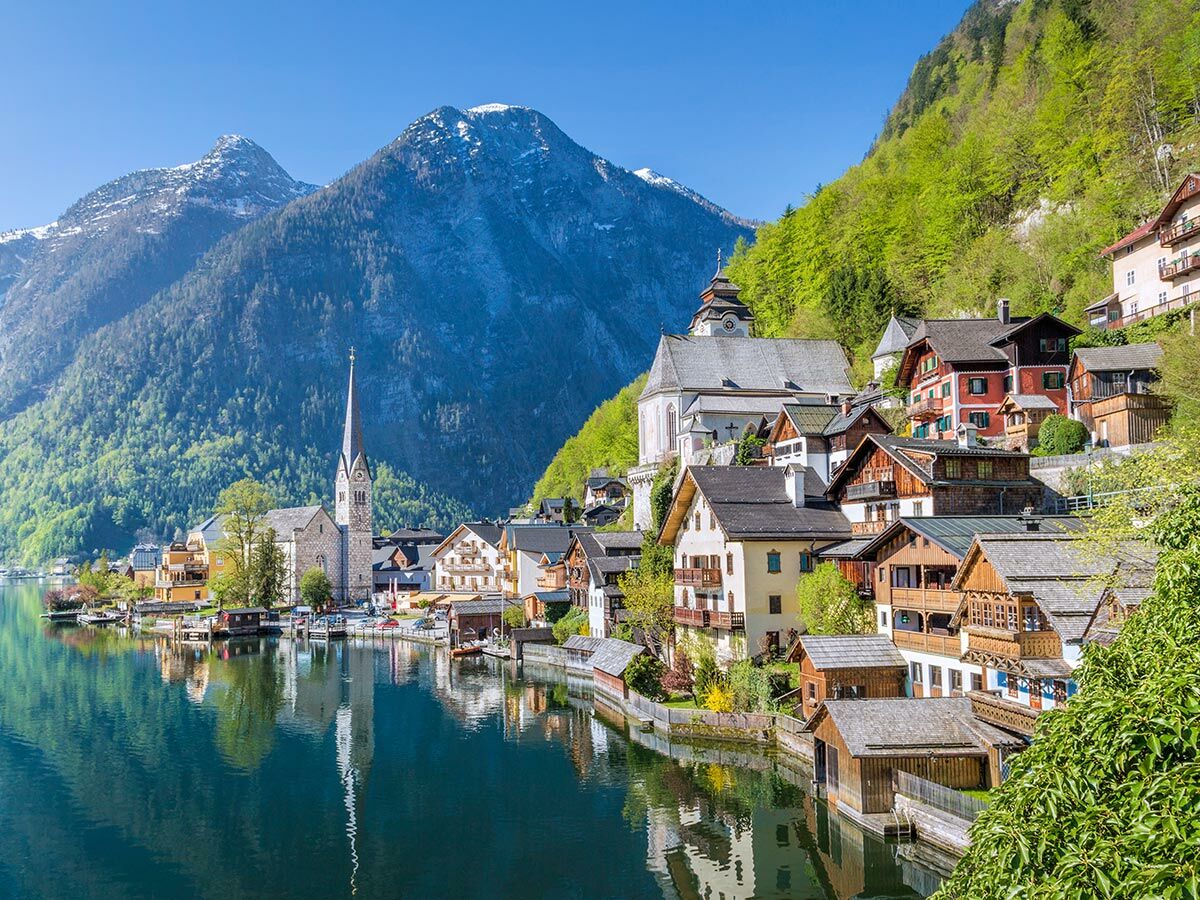 Malerisches Dorf Hallstatt am Hallstätter See mit Kirche, traditionellen Häusern und schneebedeckten Alpen im Hintergrund.