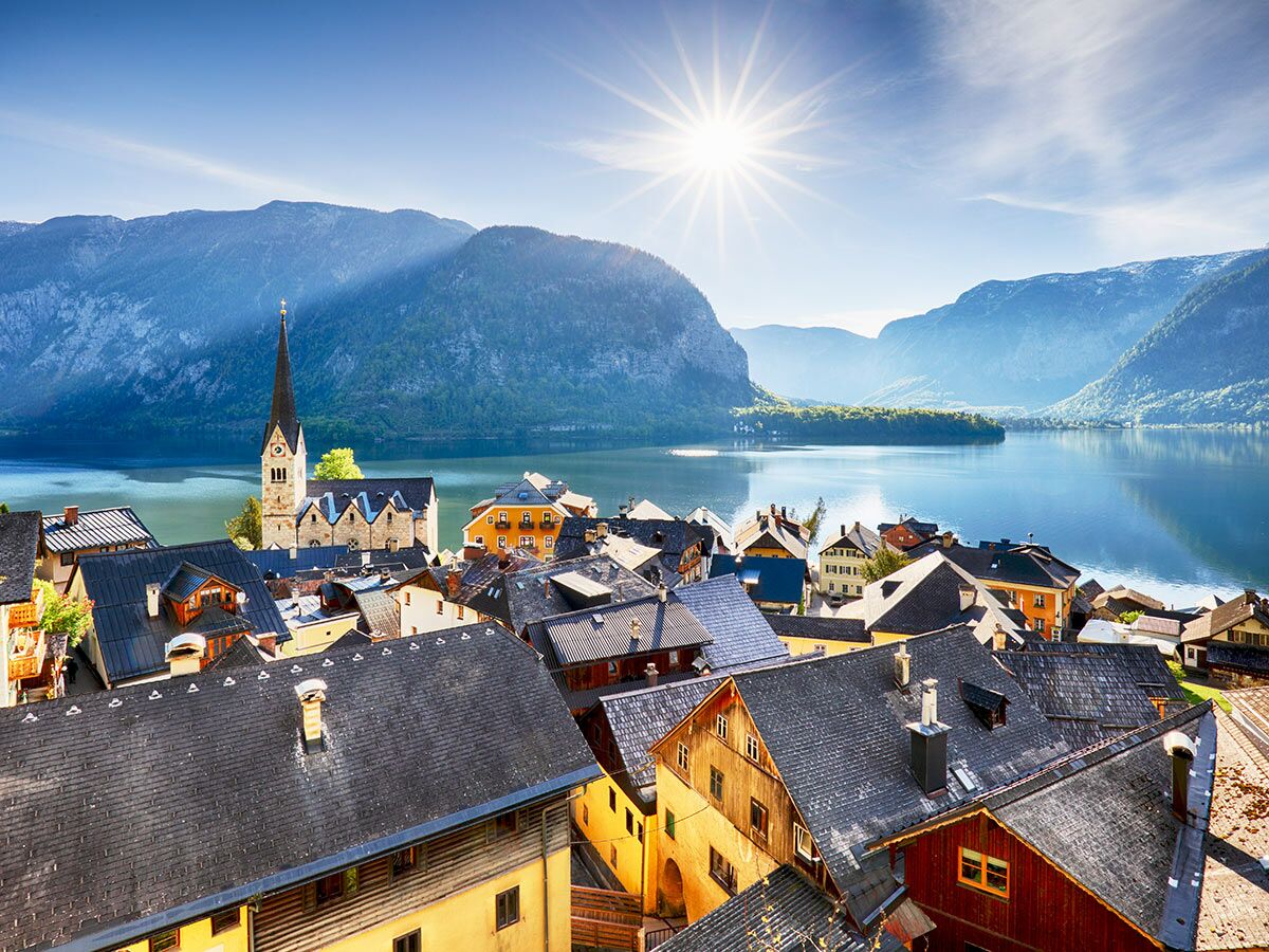 Malerisches Hallstatt Dorf am See, umgeben von Alpenbergen unter strahlendem Sonnenschein, mit markantem Kirchturm.