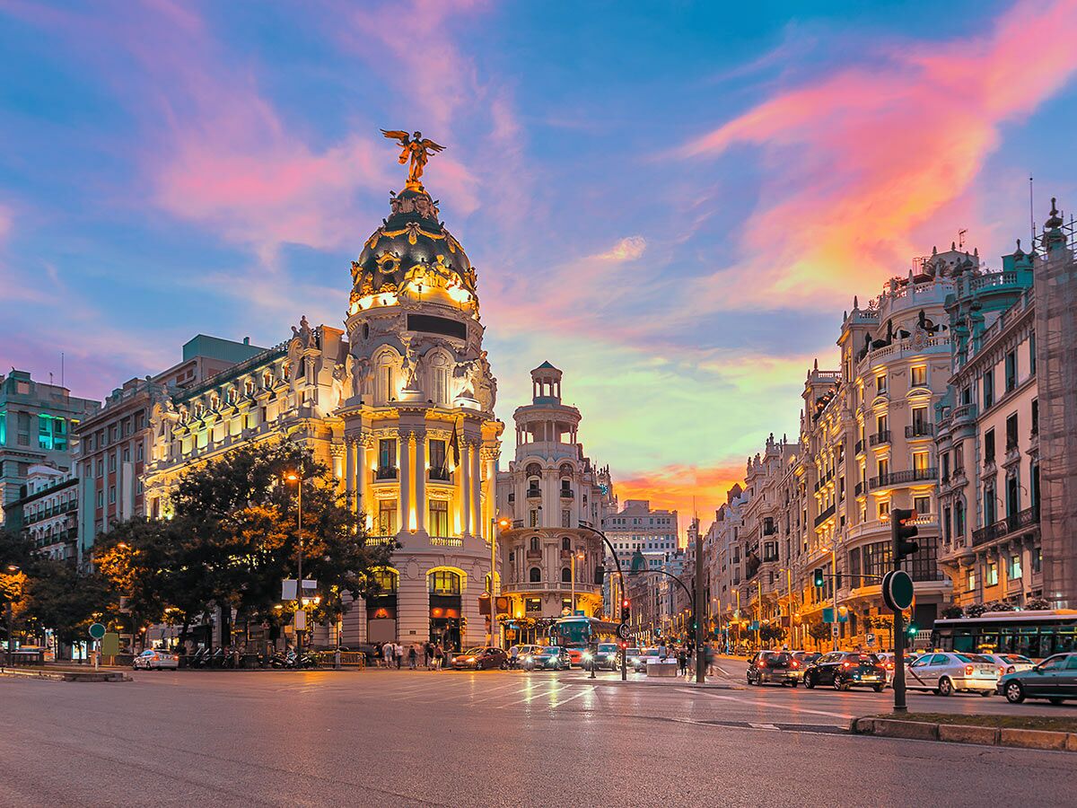 Das ikonische Metrópolis Gebäude in Madrid bei Sonnenuntergang mit lebhaften Wolken, geschäftiger Straße und historischen Fassaden.