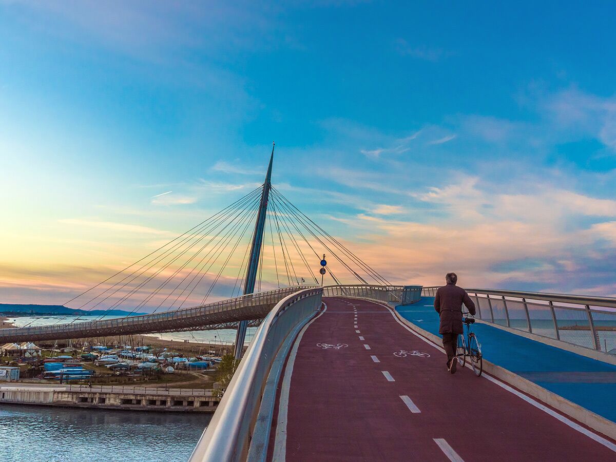 Moderne Schrägseilbrücke bei Sonnenuntergang, ein Radfahrer geht mit seinem Fahrrad auf einem speziellen Radweg über das Meer.
