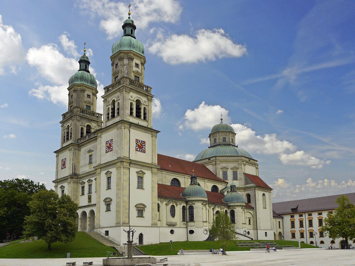 Imposante barocke Klosterkirche mit zwei hohen Türmen, grünen Kuppeln und einem großen Hauptgebäude unter blauem Himmel mit Wolken.