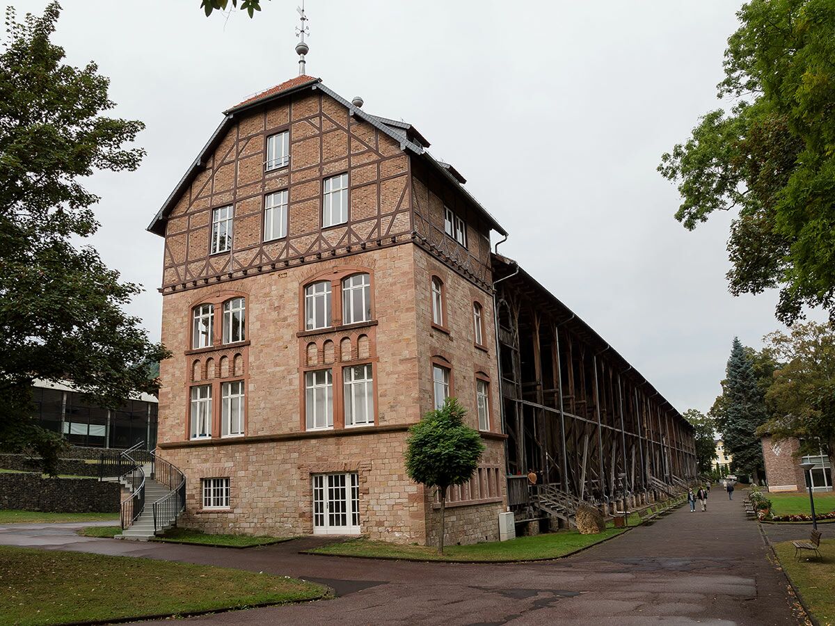 Historisches Gebäude mit Fachwerk und langem Holz-Gradierwerk in einem Kurpark an einem bewölkten Tag.