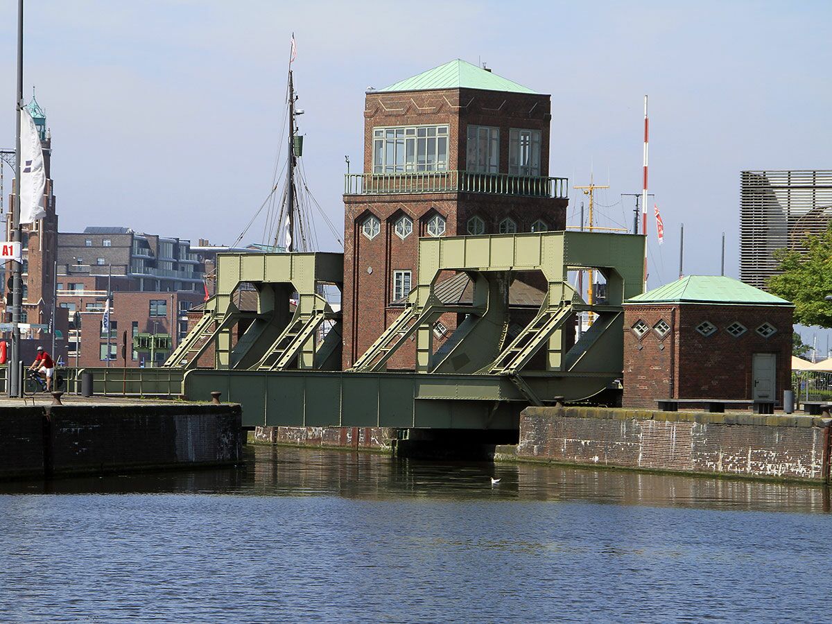 Historische Klappbrücke und Kontrollturm im Hafen mit Ziegelgebäuden, grünem Dach und Wasserweg.