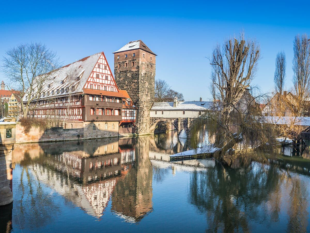 Historisches Nürnberg: Winterlandschaft mit verschneitem Weinstadel, Henkersteg und Wasserturm an der Pegnitz unter blauem Himmel.