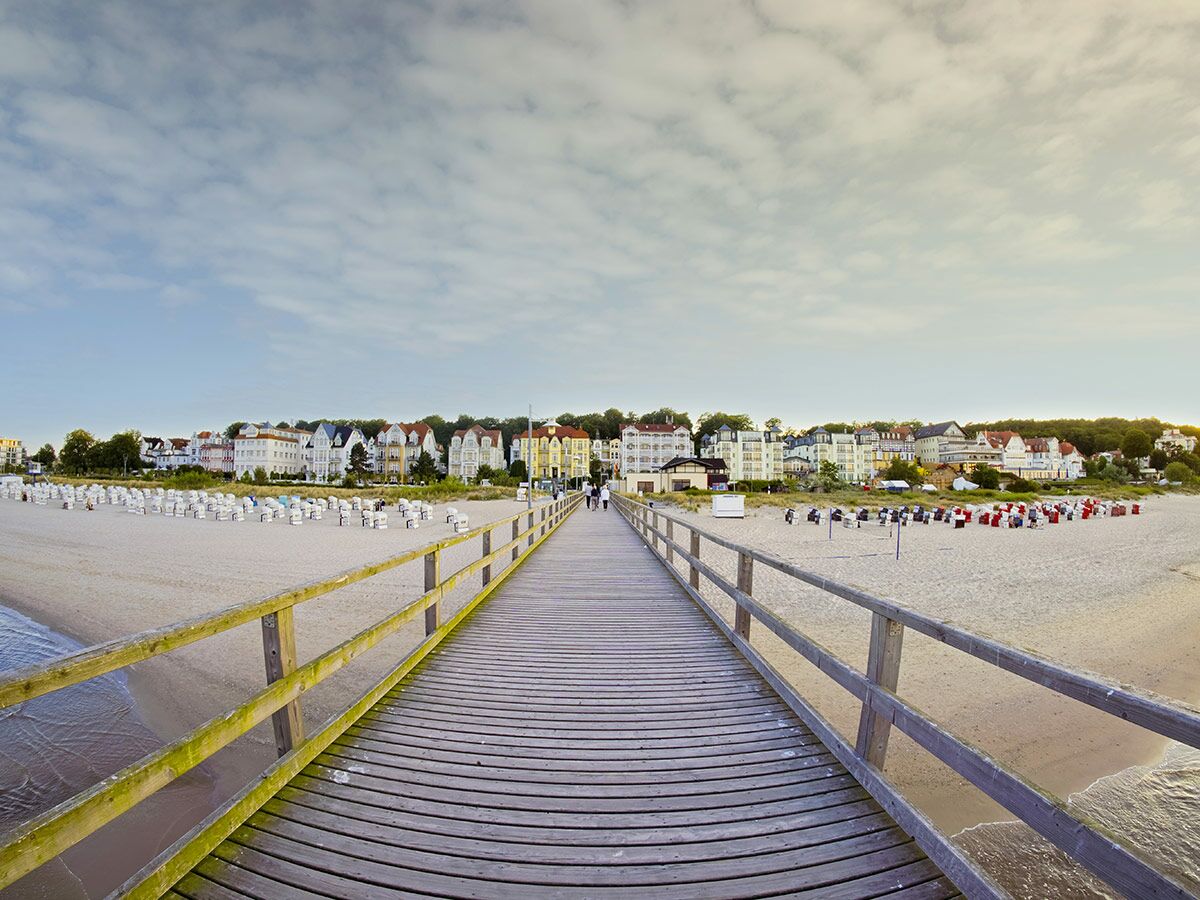 Holzseebrücke führt zu einem Sandstrand mit vielen Strandkörben und historischen Gebäuden einer Küstenstadt.