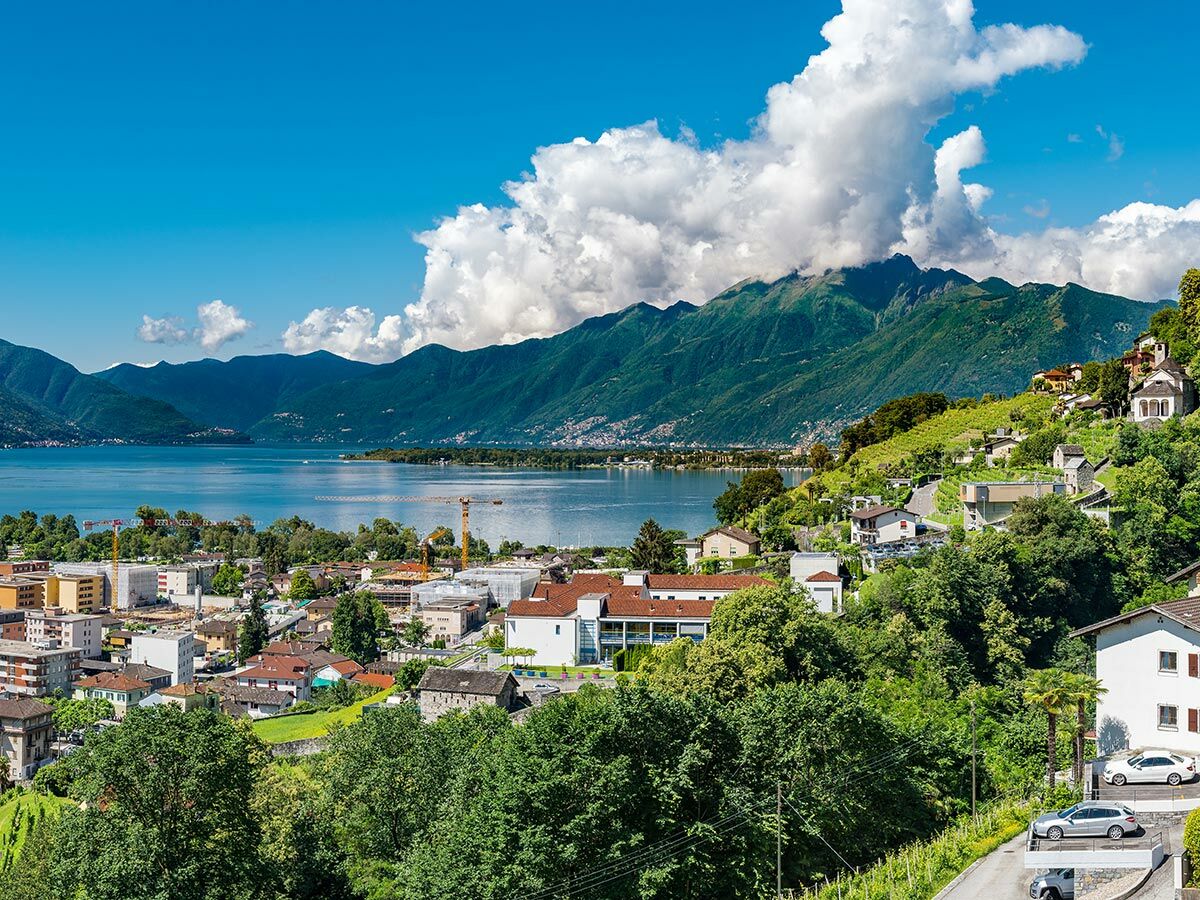 Panoramablick auf eine Stadt am blauen Bergsee, umgeben von grünen Bergen unter blauem Himmel mit Wolken, ideal für Reisen.