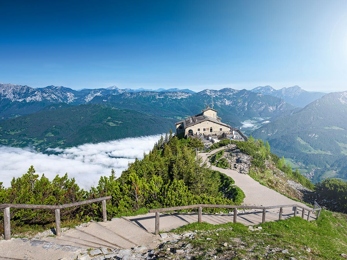 Das Kehlsteinhaus auf einem sonnigen Berggipfel mit Panoramablick über die bayerischen Alpen und Wolkenmeer im Tal, Wanderweg.