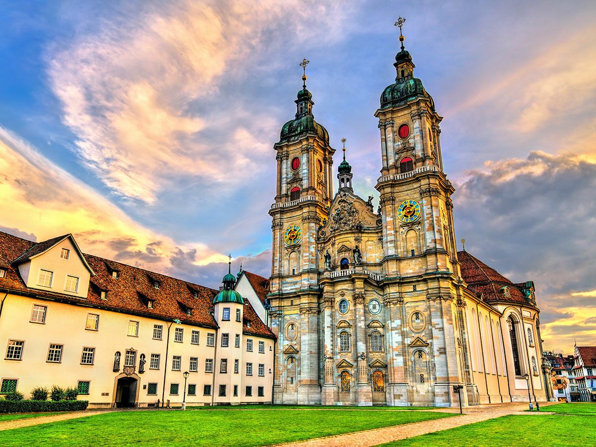 Die barocke Stiftskirche St. Gallen mit zwei Türmen und Uhren bei Sonnenuntergang, umgeben von historischen Gebäuden.