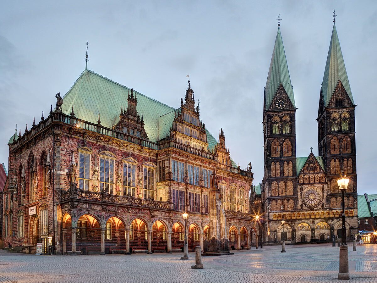 Bremen Marktplatz bei Dämmerung mit beleuchtetem historischen Rathaus und St. Petri Dom mit hohen Türmen und Uhr.