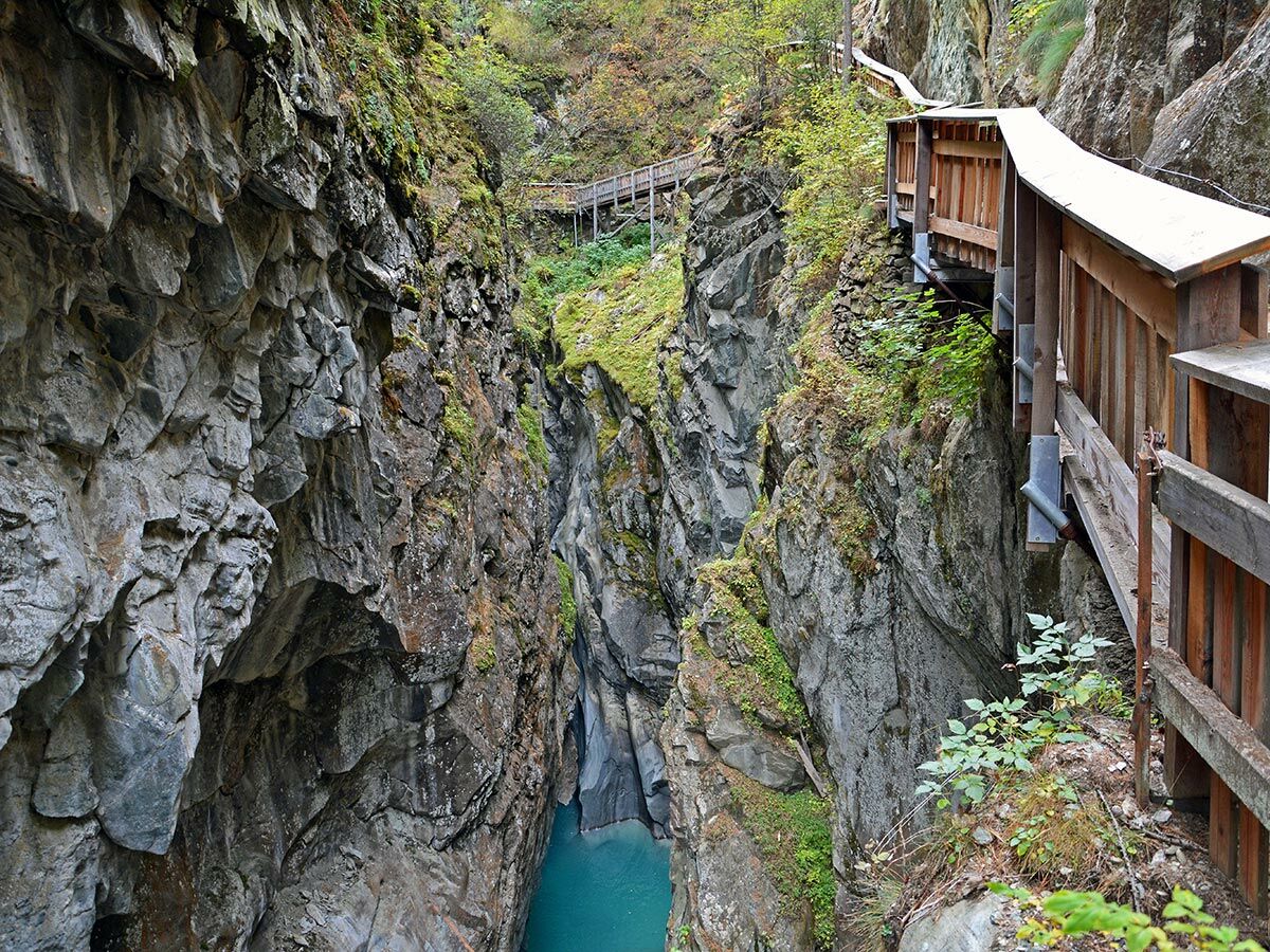 Tiefe Schlucht mit steilen Felswänden, türkisfarbenem Fluss und in den Fels gebauten hölzernen Wanderwegen und Stegen.