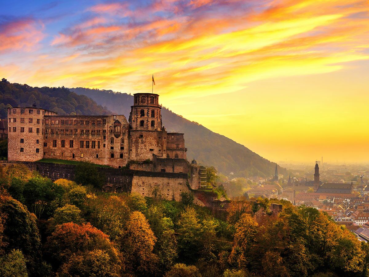 Historisches Heidelberger Schloss bei Sonnenuntergang, umgeben von herbstlichen Bäumen, mit Blick auf die Stadt Heidelberg.