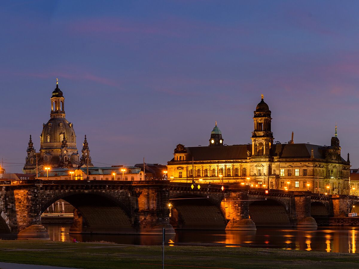 Beleuchtete Dresdner Altstadt mit Frauenkirche, Augustsbrücke und Elbreflexionen bei Dämmerung, blaue Stunde.