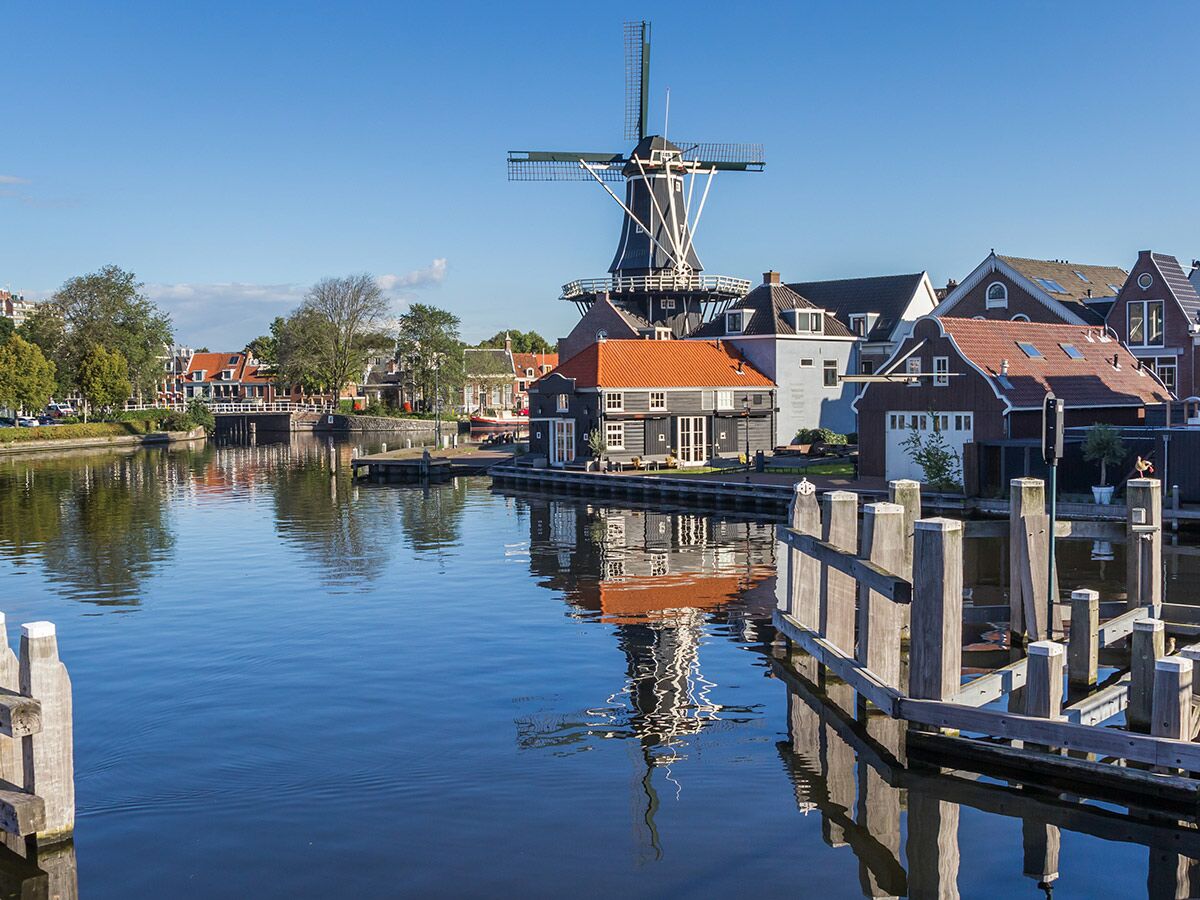 Die historische Windmühle De Adriaan in Haarlem, Niederlande, steht majestätisch am Ufer eines ruhigen Kanals mit Häusern.