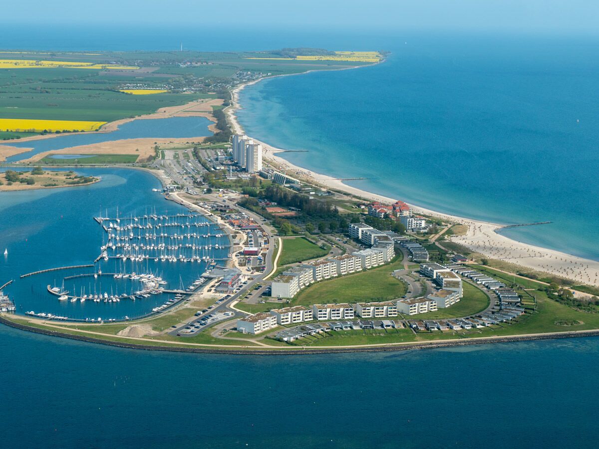 Luftaufnahme einer lebhaften Küstenstadt mit großem Yachthafen voller Boote, breitem Sandstrand und vielen Hotelgebäuden.