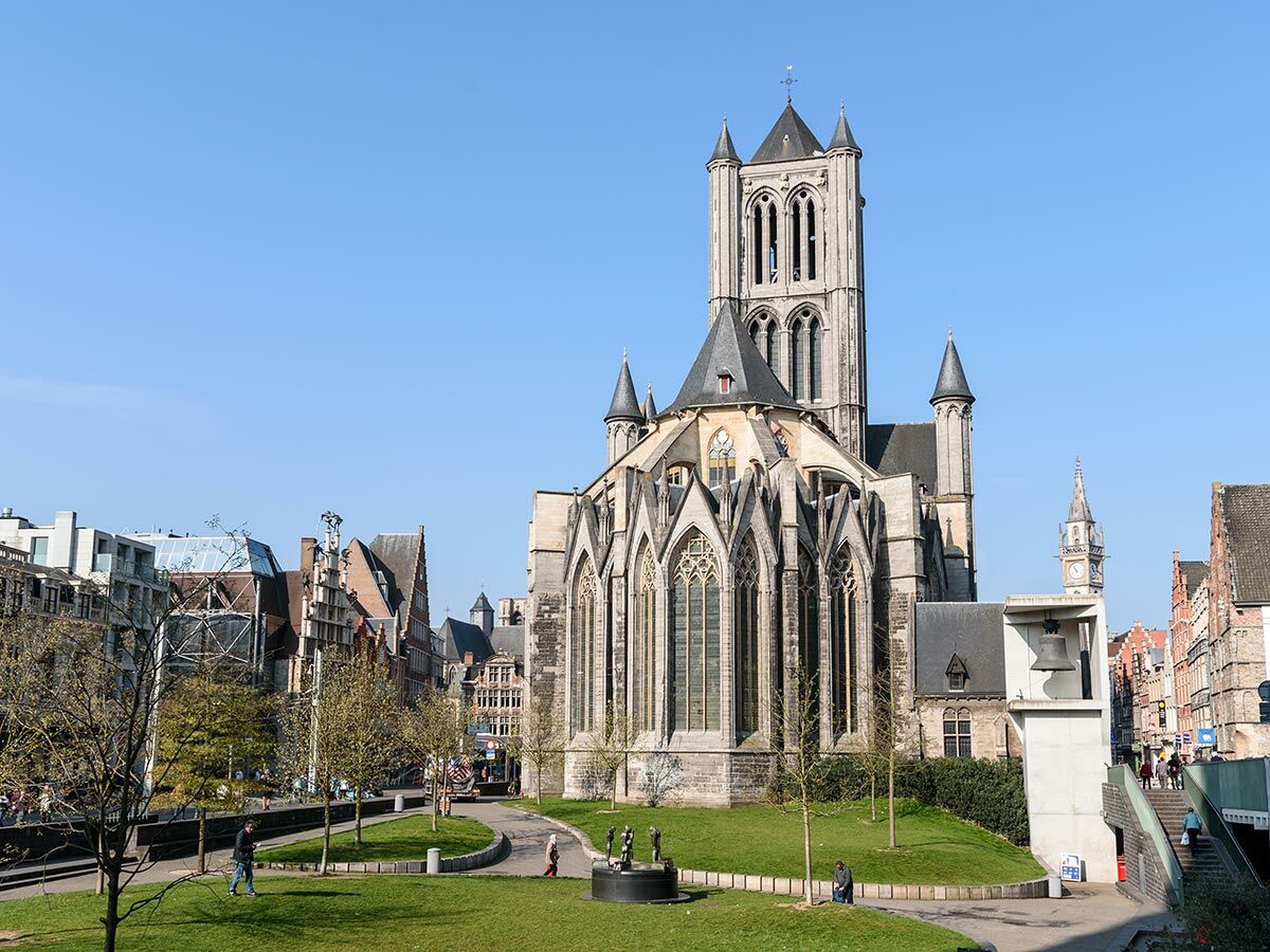 Gotische St. Nikolaus Kirche in Gent, Belgien, an einem sonnigen Tag mit blauem Himmel und Grünfläche im Vordergrund.