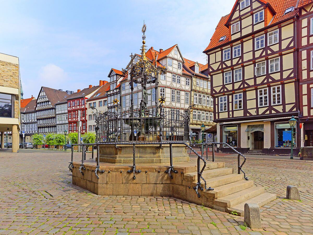 Historischer Marktbrunnen auf einem Kopfsteinpflasterplatz umgeben von traditionellen deutschen Fachwerkhäusern unter blauem Himmel.