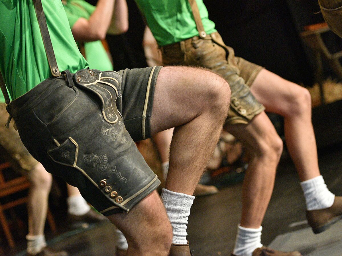 Gruppe Männer in traditionellen Lederhosen und grünen Hemden tanzt Volkstanz, Beine und Tracht im Fokus, Oktoberfest Atmosphäre.
