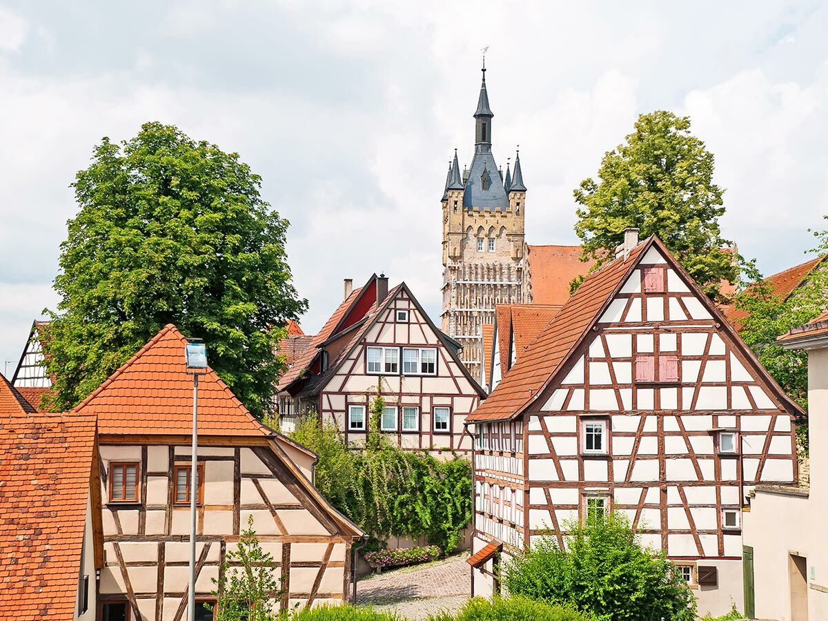 Malerische deutsche Altstadtansicht mit traditionellen Fachwerkhäusern, roten Dächern und historischem Kirchturm unter blauem Himmel.