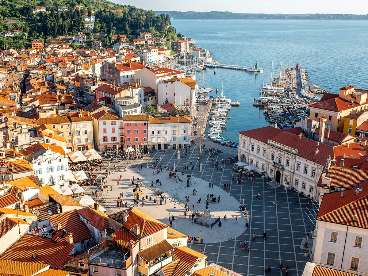 Luftbild der slowenischen Küstenstadt Piran mit Tartini-Platz, belebtem Hafen, Altstadt und Adria-Meer.