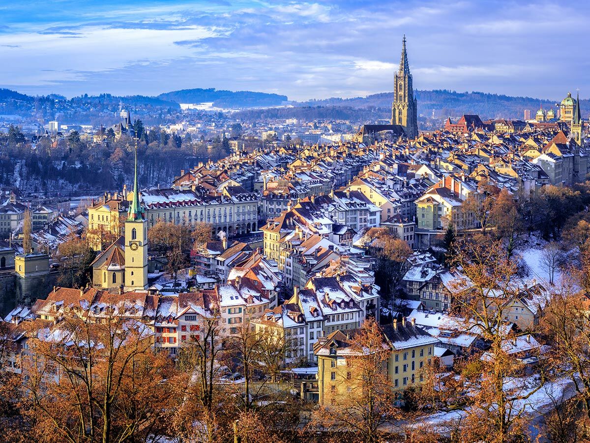 Verschneite Berner Altstadt im Winter mit historischen Gebäuden, Kirchen und Aare. Panoramablick bei Sonnenlicht.
