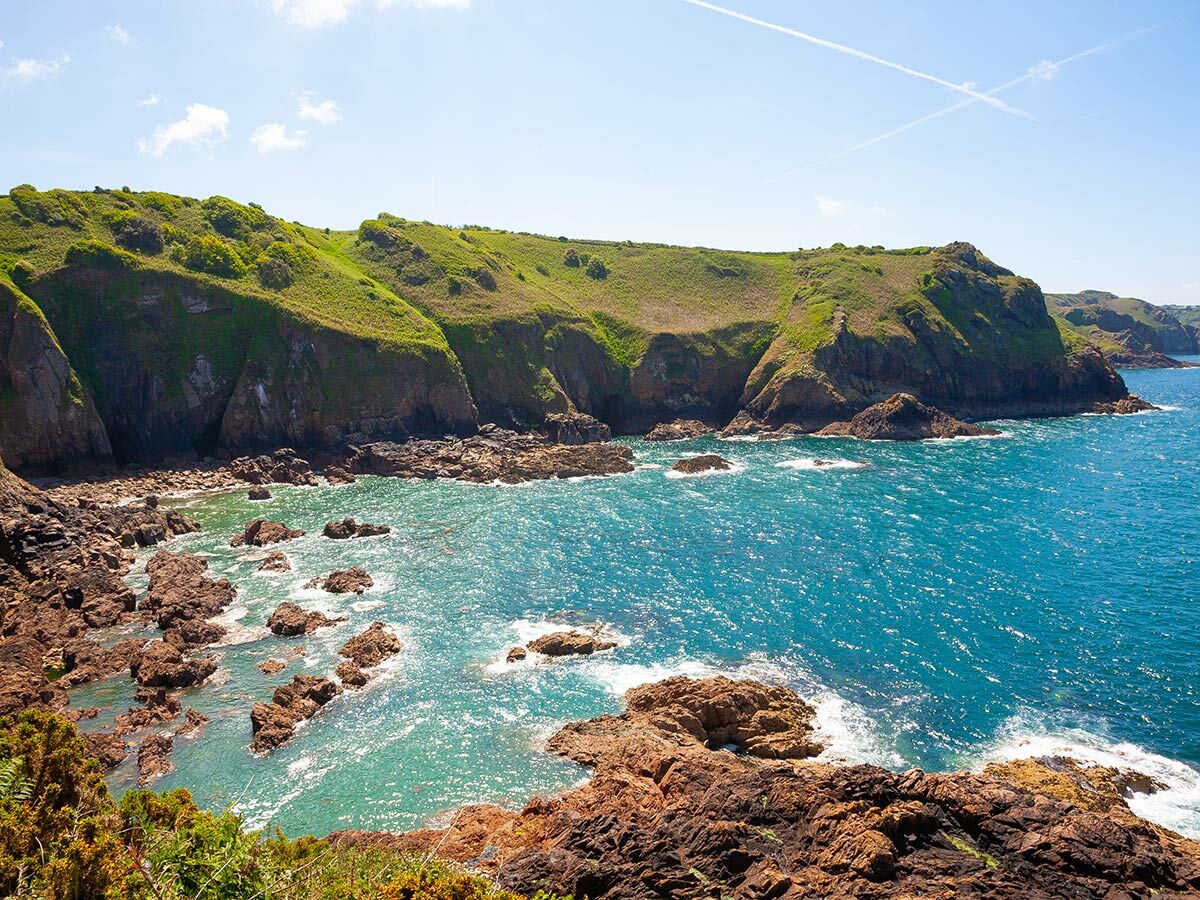 Malerische Küste mit grünen Klippen, felsigen Buchten und azurblauem Meer unter strahlend blauem Himmel.