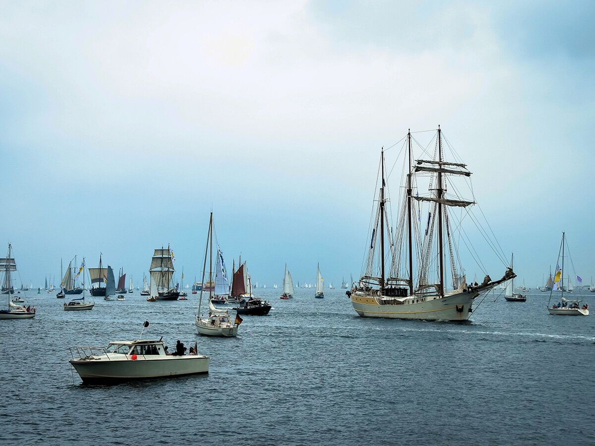 Ein großes Segelschiff führt eine Flotte von Booten auf dem Meer bei bewölktem Himmel an.