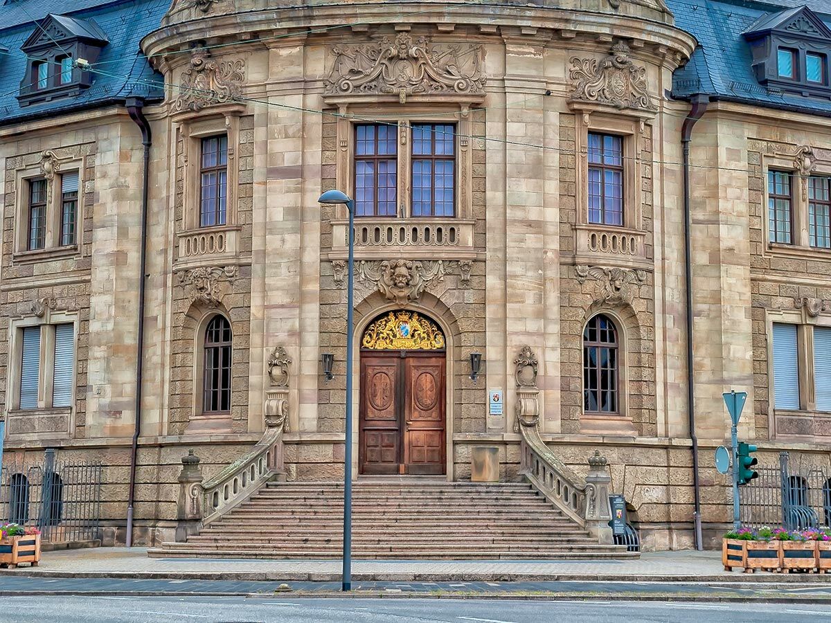 Prächtige Sandstein-Fassade eines historischen Gebäudes mit großem Holzeingang, verzierten Treppen und Fenstern.
