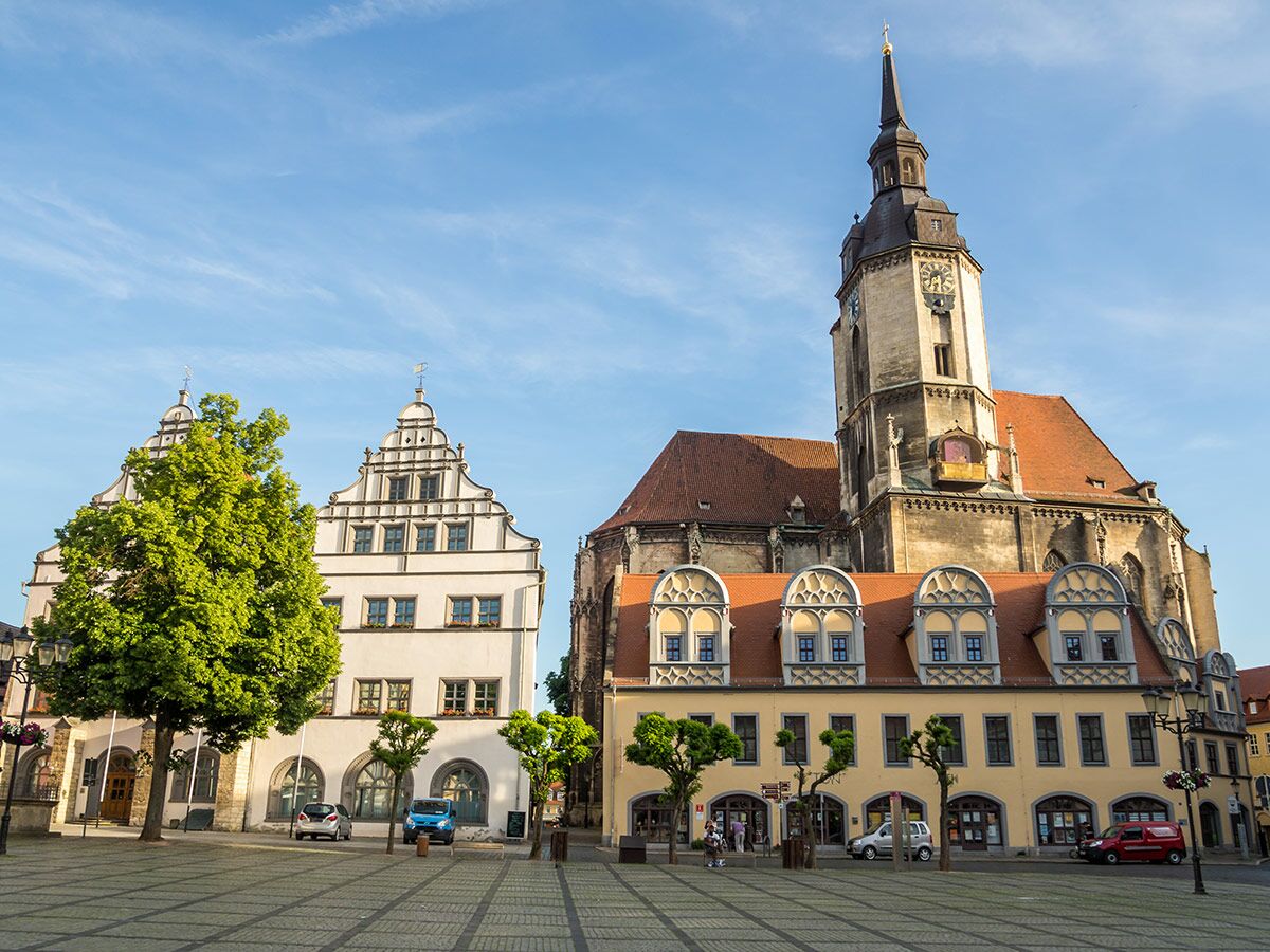 Historischer Marktplatz mit großer Kirche, Turm, Giebelhäusern und gelbem Gebäude unter blauem Himmel in deutscher Stadt.