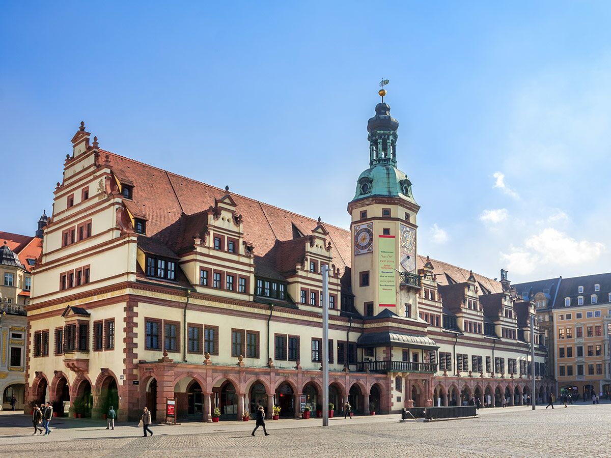 Das Alte Rathaus in Leipzig mit seinem markanten Turm am sonnigen Marktplatz, umgeben von Fußgängern.