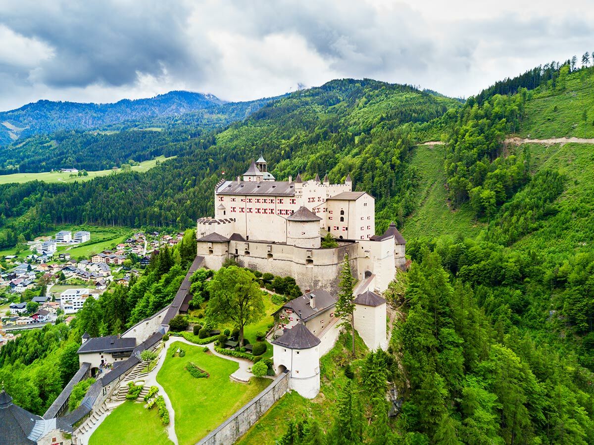 Luftbild der mittelalterlichen Festung Hohenwerfen in Österreich, umgeben von grünen Wäldern, Bergen und einem Dorf im Tal.