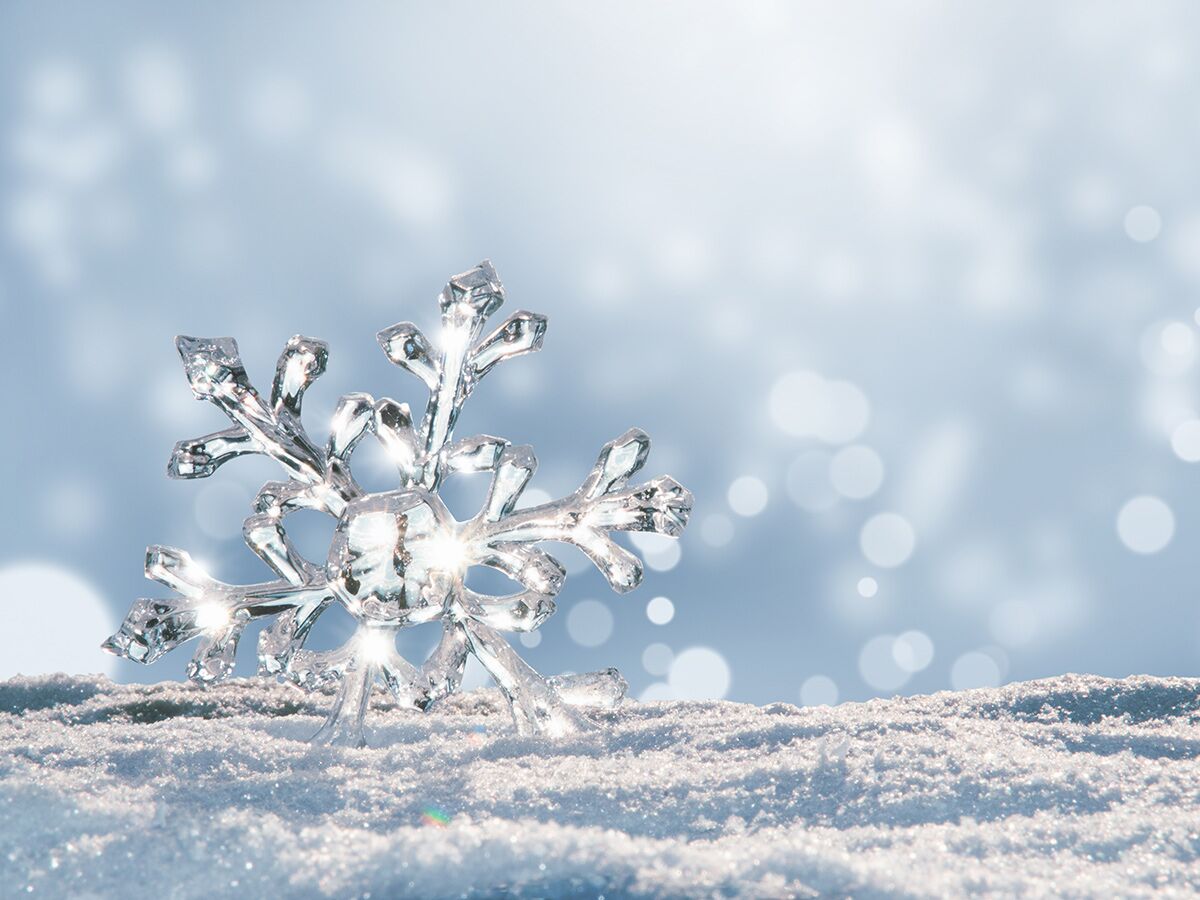 Glitzernde Eiskristall-Schneeflocke auf frischem Schnee mit verschwommenem Bokeh-Hintergrund in Hellblau. Symbol für Winter und Weihnachten.