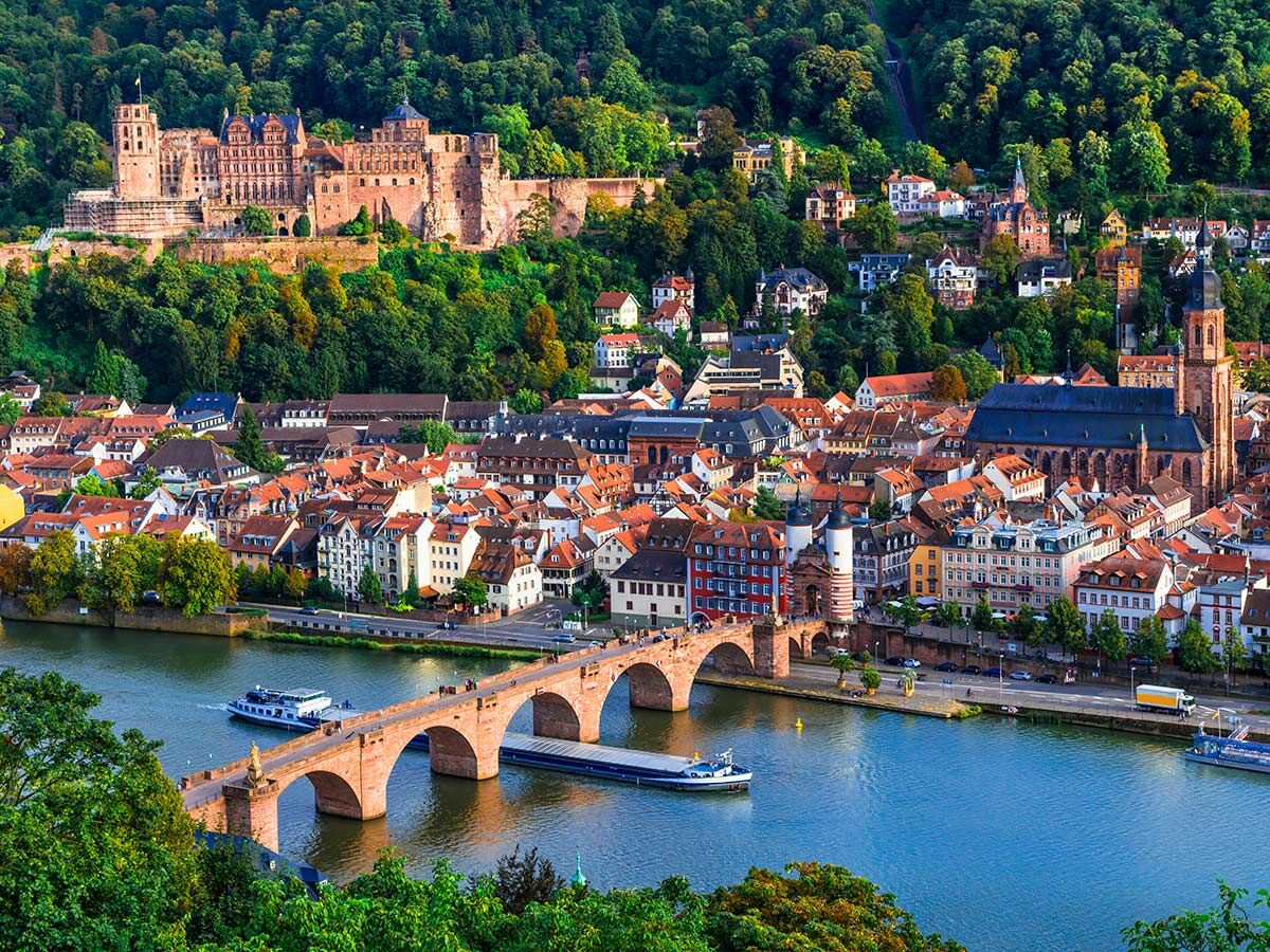 Panorama von Heidelberg mit historischem Schloss, der Altstadt, der Alten Brücke über den Neckar und grünen Hügeln.