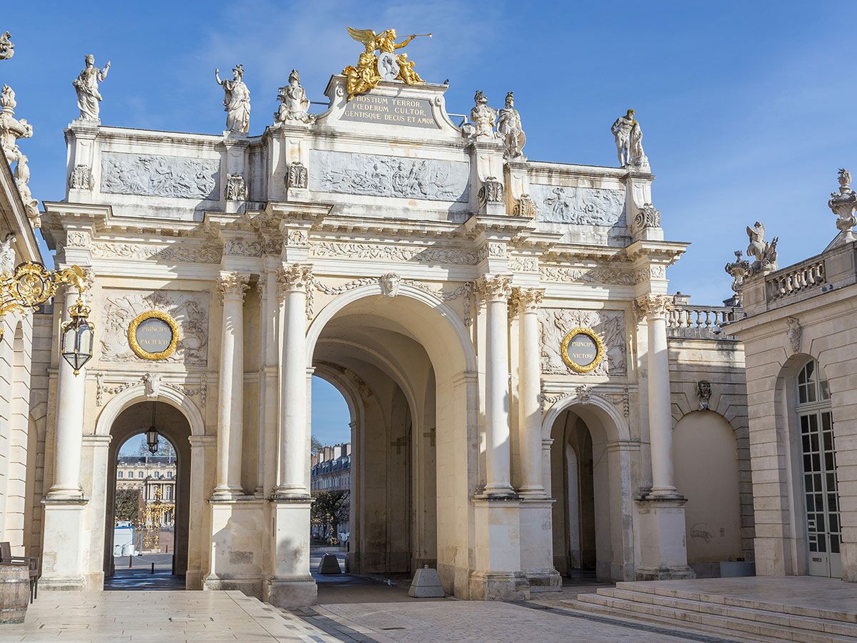 Prächtiger Arc Héré in Nancy, Frankreich, mit barocken Verzierungen, Statuen und goldenen Akzenten unter blauem Himmel.