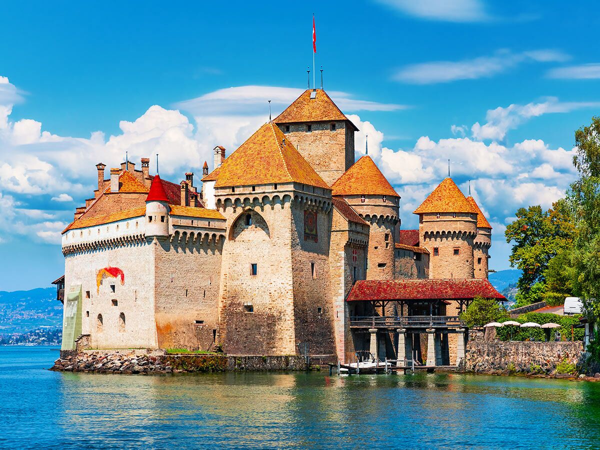 Historisches Chillon Schloss am Ufer des Genfersees in der Schweiz, mit Türmen, roten Dächern und blauem Himmel.