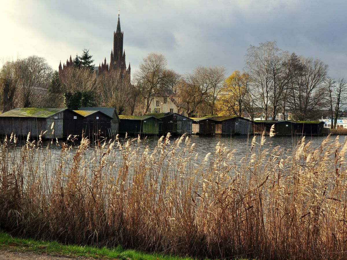 Gotische St. Gotthardt-Kirche über Bootshäusern und Schilf am Fluss Havel in Brandenburg. Herbstliche Landschaft.