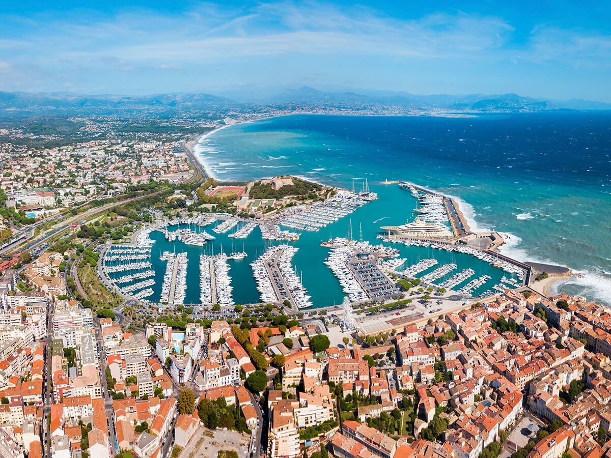Luftaufnahme der Küstenstadt Antibes mit geschäftigem Yachthafen, Superyachten, Strand und Mittelmeer in Frankreich.