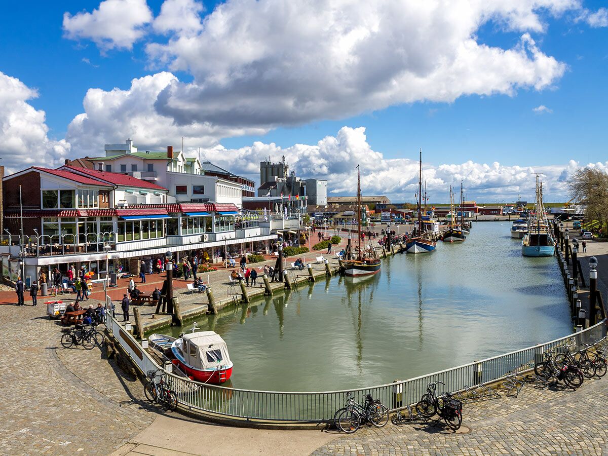 Ein sonniger Tag an einer belebten Hafenpromenade mit Restaurants, Menschen und traditionellen Fischerbooten im Kanal.